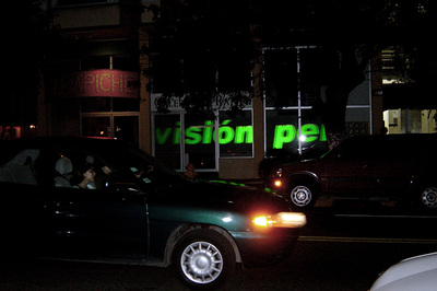 green words (hard to read) projected on storefront glass at night, passing car