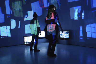 two people inside a blue room with projected rectangles and three flat screens